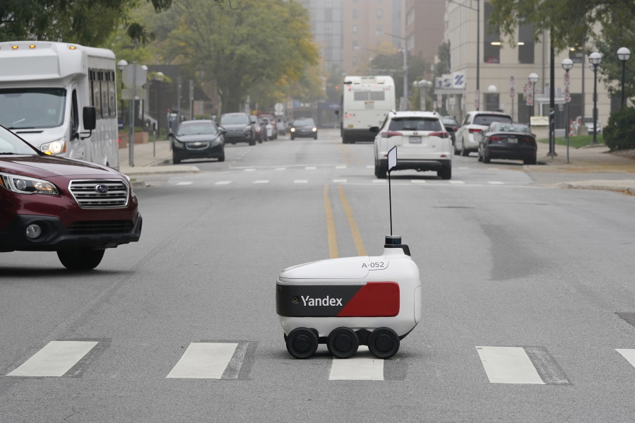 A food delivery robot crosses a street in Ann Arbor, Mich. on Thursday, Oct. 7, 2021. Robot food delivery is no longer the stuff of science fiction. Hundreds of little robots ---- knee-high and able to hold around four large pizzas ---- are now navigating college campuses and even some city sidewalks in the U.S., the U.K. and elsewhere. While robots were being tested in limited numbers before the coronavirus hit, the companies building them say pandemic-related labor shortages and a growing preference for contactless delivery have accelerated their deployment.