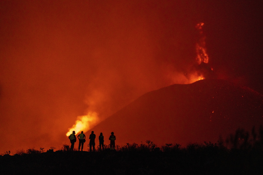Police officers and emergency personnel look as lava flows from a volcano as it continues to erupt on the Canary island of La Palma, Spain, Tuesday, Nov. 2, 2021. A volcano on the Spanish island of La Palma that has been erupting for six weeks has spewed more ash from its main mouth a day after producing its strongest earthquake to date.