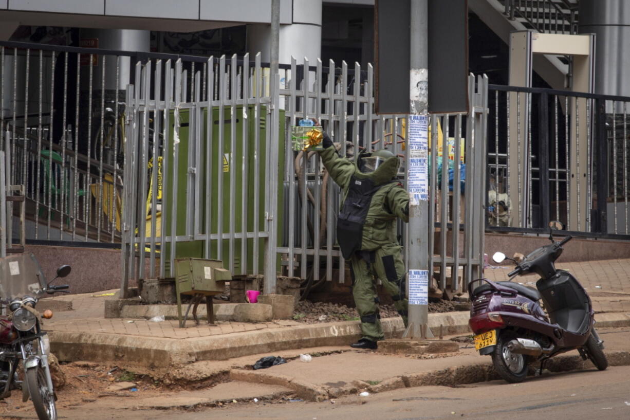 A bomb disposal officer examines a suspicious package resembling a gift before subjecting it to a controlled explosion, next to the central police station in Kampala, Uganda, Tuesday, Nov. 16, 2021. Two loud explosions rocked Uganda's capital, Kampala, early Tuesday, sparking chaos and confusion as people fled what is widely believed to be coordinated attacks.