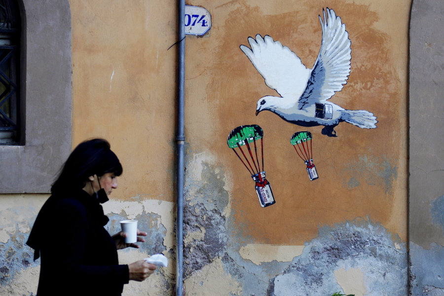 FILE -  A woman walks past a mural depicting a white dove parachuting COVID-19 vaccine vials, posted near the Italian Health Ministry Headquarters in Rome, April 4, 2021. The pandemic is again roaring across parts of Western Europe, a prosperous region with relatively high vaccination rates and good health care systems but where lockdown measures to rein in the virus are largely a thing of the past. Italy, an early victim of the pandemic, has a high vaccination rate, but is also seeing numbers edge higher, which experts believe is due to vaccine efficacy wearing off.