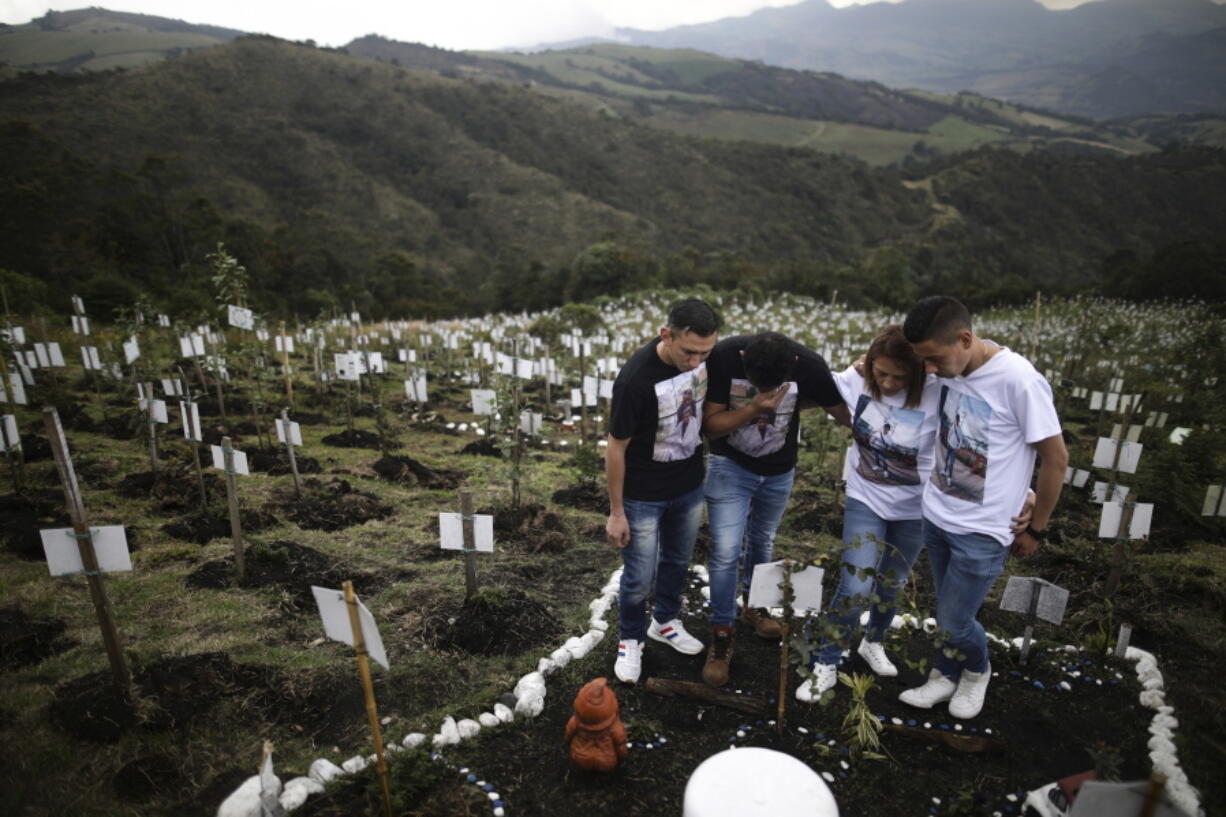Relatives of Luis Enrique Rodriguez, who died of COVID-19, visit where he was buried on a hill at the El Pajonal de Cogua Natural Reserve, in Cogua, north of Bogota, Colombia, Monday, Oct. 25, 2021. Rodriguez died May 14, 2021. Relatives bury the ashes of their loved ones who died of coronavirus and plant a tree in their memory.