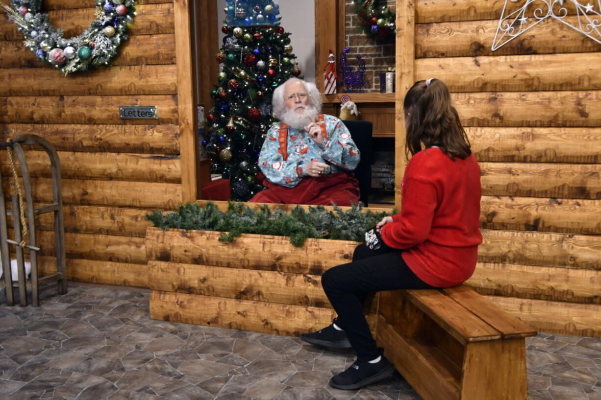 Santa Claus, portrayed by Sid Fletcher, sits behind a glass barrier as he listens to Kendra Alexander of St. James, Minn., during her Nov. 15 visit to The Santa Experience at the Mall of America in Bloomington, Minn. A microphone in the greens picks up conversation.