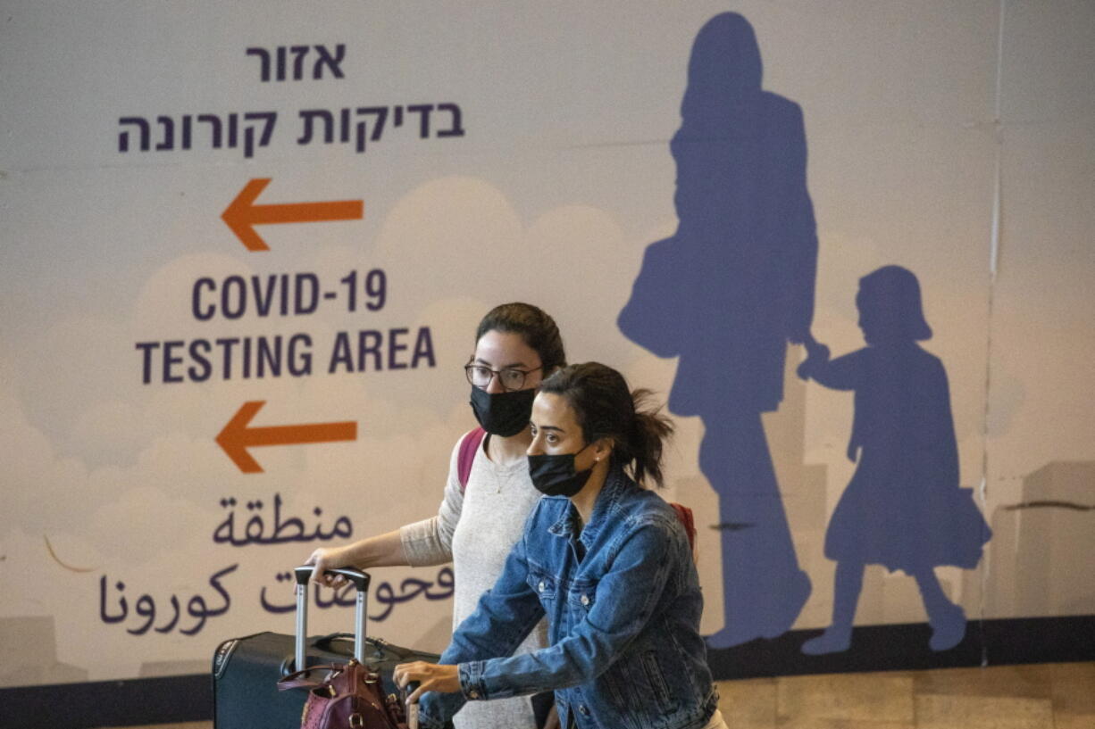 Travelers wearing protective face masks arrive at Ben Gurion Airport near Tel Aviv, Israel, Sunday, Nov. 28, 2021. Israel on Sunday approved barring entry to foreign nationals and the use of controversial technology for contact tracing as part of its efforts to clamp down on a new coronavirus variant.