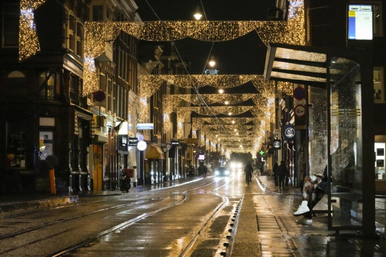 A lone person waits for a tram in a near-deserted street full of closed restaurants, bars and shops Friday in Amsterdam, Netherlands. The Dutch government tightened its lockdown Friday night amid swiftly rising infections and ICU admissions.