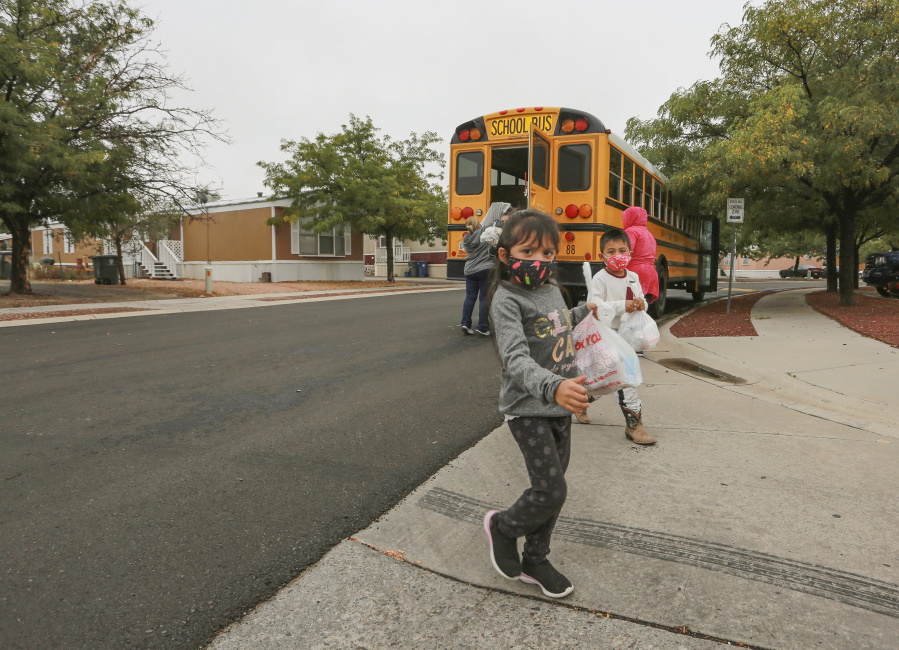 FILE - Kindergarteners who are learning remotely during the coronavirus pandemic pick up meals at a bus stop near their home in Santa Fe, N.M., on Sept. 9, 2020. The Santa Fe school district decided last week to close its doors Tuesday, Nov. 23, 2021, and pivot to remote learning in a bid to reduce virus outbreaks ahead of the Thanksgiving holiday.