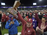 Washington State acting head coach Jake Dickert, center, holds up the Apple Cup Trophy after it was presented to him by Washington Gov. Jay Inslee, left, after Washington State beat Washington 40-13 in an NCAA college football game, Friday, Nov. 26, 2021, in Seattle. (AP Photo/Ted S.