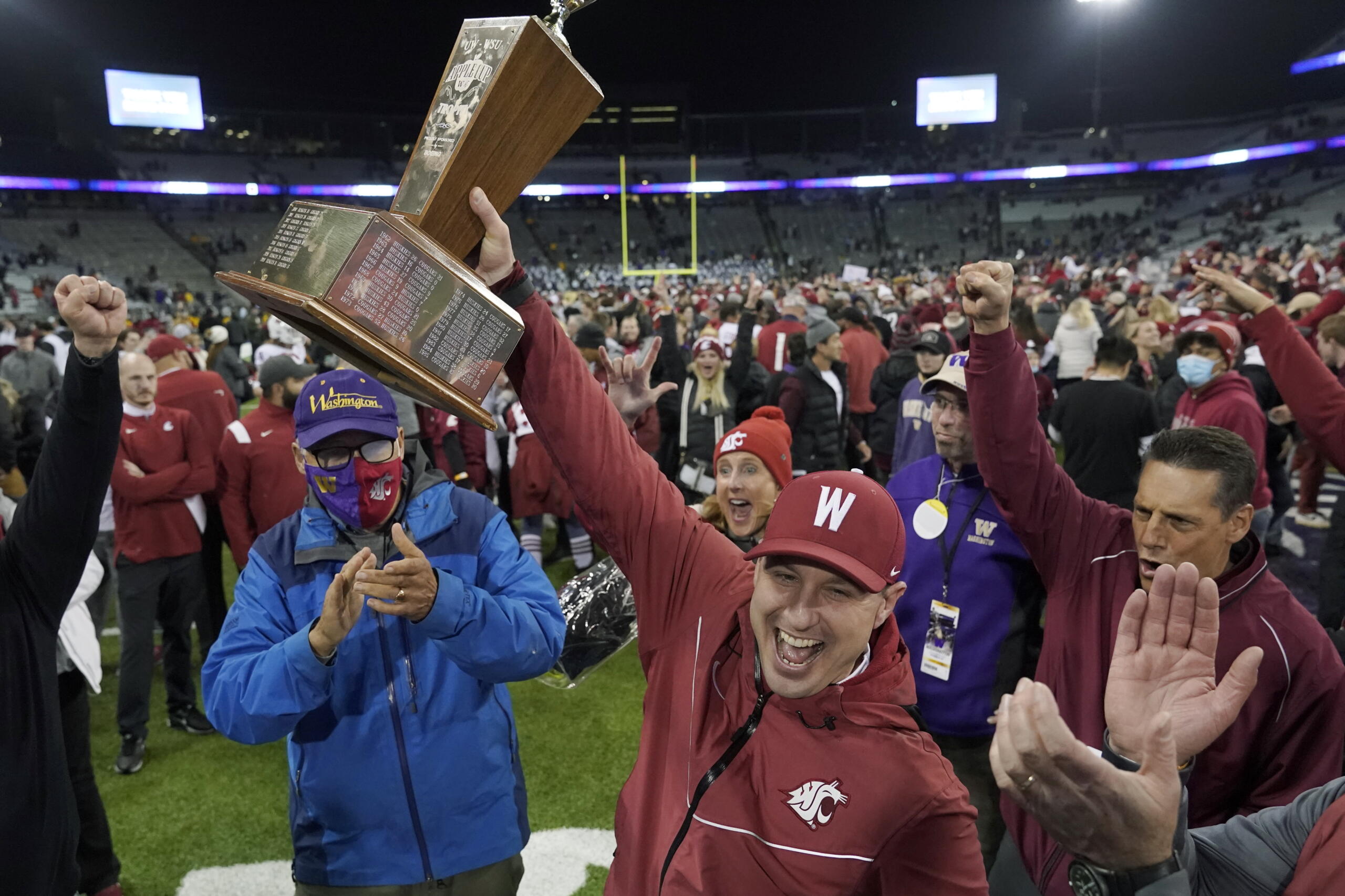 Washington State acting head coach Jake Dickert, center, holds up the Apple Cup Trophy after it was presented to him by Washington Gov. Jay Inslee, left, after Washington State beat Washington 40-13 in an NCAA college football game, Friday, Nov. 26, 2021, in Seattle. (AP Photo/Ted S.