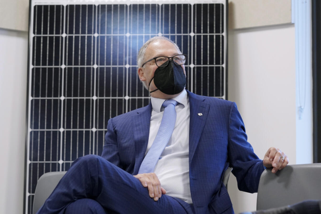 Gov. Jay Inslee sits in front of a solar panel after speaking Dec. 13 at a news conference in Olympia. (Ted S.