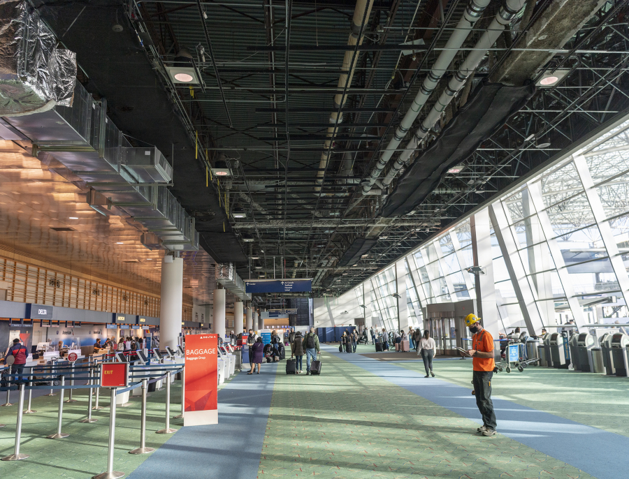 The exposed underside of the Portland International Airport roof hangs above travelers. The expanded terminal that is planned in the PDX Next project will include a new, curved roof.