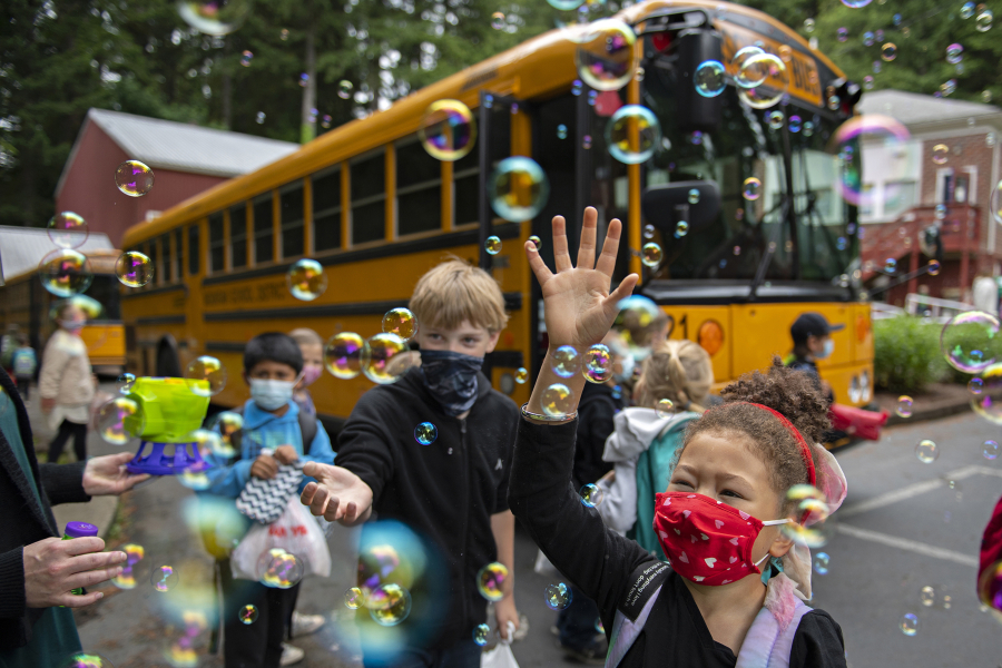 Students, including first grader Trulee Dunn, right, get a warm goodbye from teachers and staff as they prepare to board the bus on the last day of class at Green Mountain School on June 15, 2021. It is tradition for teachers and staff to blow bubbles to bid farewell to the children, but this year a bubble machine was used as a COVID-19 precaution.