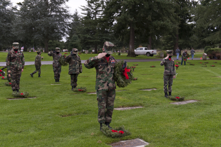 Young Marines Sgt. Gabriel Blok, 16, lays a wreath and salutes the grave of a veteran Saturday at Evergreen Memorial Gardens in Vancouver.  At top,  Lewis & Clark Young Marines practice folding the flag before the official ceremonies begin.