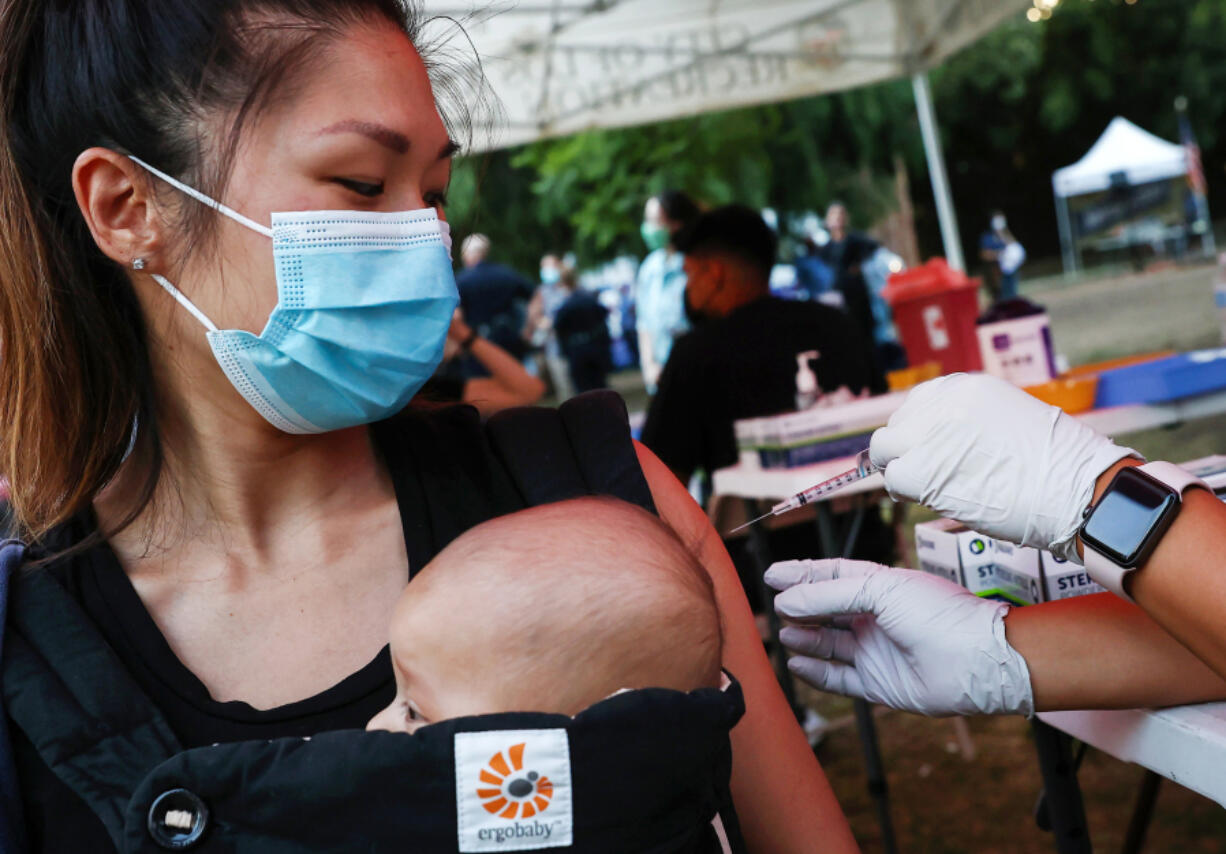 A person receives a COVID-19 vaccination dose, while carrying a baby in tow, as part of a National Night Out event hosted by Melrose Action on Aug. 3, 2021 in Los Angeles.