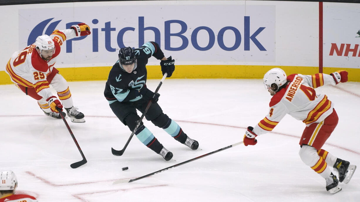 Seattle Kraken center Morgan Geekie, center, drives between Calgary Flames center Dillon Dube, left, and defenseman Rasmus Andersson during the first period of an NHL hockey game Thursday, Dec. 30, 2021, in Seattle. (AP Photo/Ted S.
