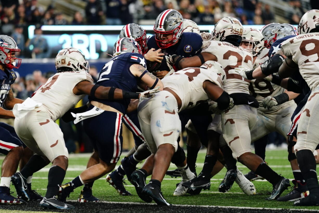 Navy quarterback Tai Lavatai, top center, runs the ball in for a touchdown during the first half of an NCAA college football game against Army, Saturday, Dec. 11, 2021, in East Rutherford, N.J.
