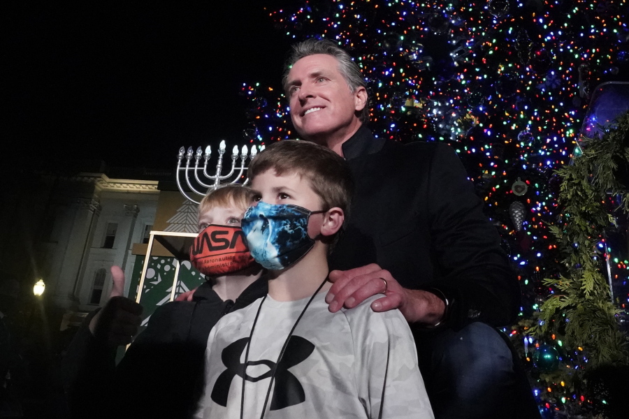 California Gov. Gavin Newsom poses for a photo with a pair of youngsters after the 90th annual State Capitol Tree Lighting Ceremony in Sacramento, Calif., Thursday, Dec. 2, 2021. Newsom has written a children's book inspired by his experiences dealing with dyslexia as a kid. The book, titled "Ben & Emma's big Hit," co-authored by Ruby Shamir, with illustrations by Alexandra Thompson, tells the story of a young boy who, with the help of a caring teacher and a friend uses baseball to cope with his dyslexia. The book is published by Philomel books and comes out Tuesday, Dec. 7.