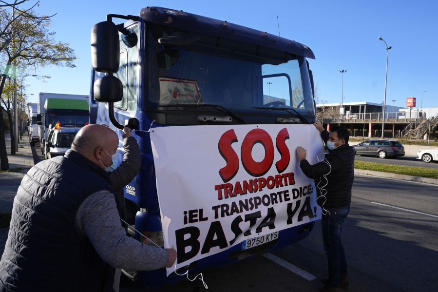 Truckers ties a banner reading 'SOS, Transport. 'That's enough' to a truck before driving slowly during a protest though Madrid, Spain, Wednesday, Dec. 15, 2021. Governments worldwide are facing protests, work stoppages or other political pressure to take action against soaring inflation. Spanish truck drivers ratcheted up the pressure by vowing a walkout days before Christmas and won relief on diesel prices, while Turkish citizens are protesting the government's unorthodox economic policies that have worsened surging inflation and made it a struggle to buy food and other goods.
