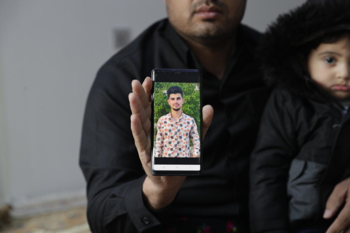 Zana Mamand, shows a photo of his missing brother, Twana Mamand, who was lost at sea in the English Channel trying to get to the UK, sits with family members, at the family house in Ranya, Iraq, Tuesday, Nov. 30, 2021. Twana had tried and failed five times to cross the English Channel from Calais before he boarded a small boat on the evening of Nov. 23.