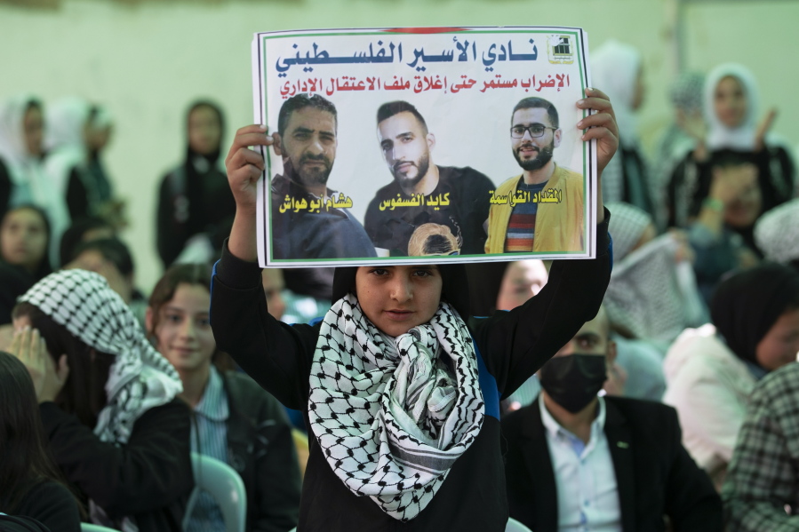 FILE - A protester holds a poster showing Kayed Fasfous, center, a Palestinian prisoner who has been on a hunger strike to protest being detained without charge by Israel, in the village of ad-Dhahiriya, near the West Bank town of Hebron, Nov. 11, 2021. A prisoner rights group said Sunday, Dec. 5, 2021, that Israel has released Fasfous, two weeks after striking a deal that ended his marathon 131-day hunger strike. Fasfous was the symbolic figurehead of six hunger strikers protesting Israel's controversial policy of "administrative detention" that allows suspects to be held indefinitely without charge for months and even years.