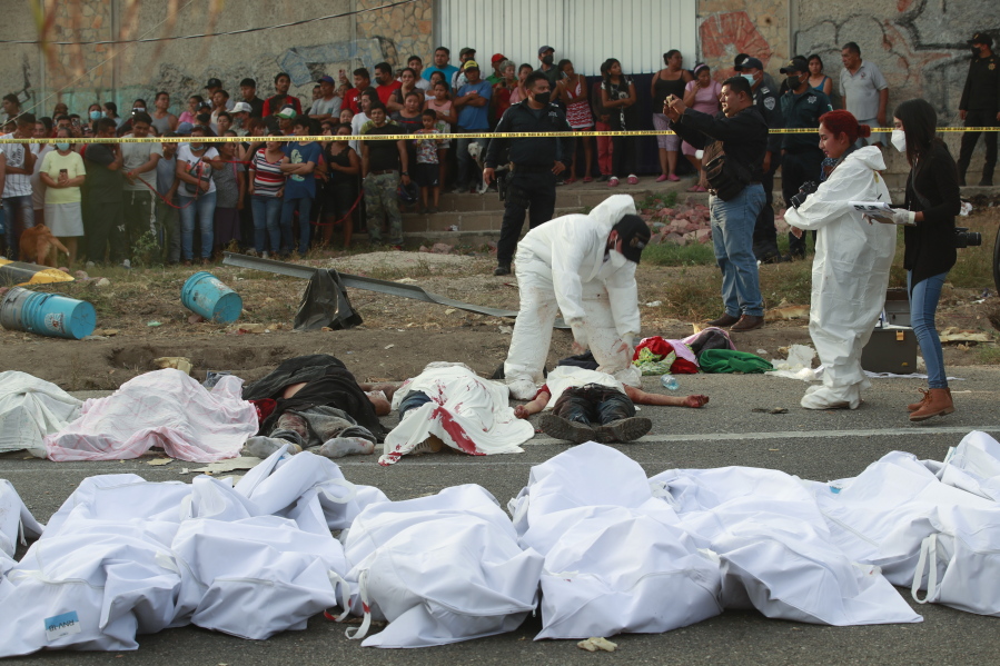 Bodies in bodybags are placed on the side of the road after an accident in Tuxtla Gutierrez, Chiapas state, Mexico, Dec. 9, 2021. Mexican authorities say at least 49 people were killed and dozens more injured when a cargo truck carrying Central American migrants rolled over on a highway in southern Mexico.