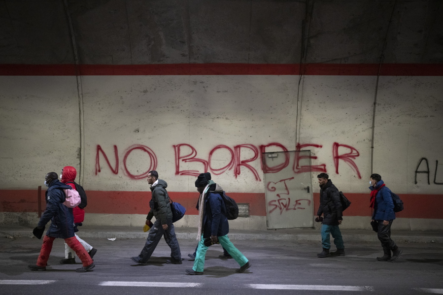 Migrants headed to France from Italy walk by a grafitti that reads "No Border" in a tunnel leading to the French-Italian border, Saturday, Dec. 11, 2021.
