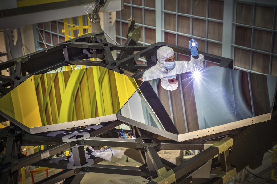 In this Sept. 29, 2014 photo made available by NASA, James Webb Space Telescope Optical Engineer Larkin Carey examines two test mirror segments on a prototype at the Goddard Space Flight Center's giant clean room in Greenbelt, Md. Webb will attempt to look back in time 13.7 billion years, a mere 100 million years after the universe-forming Big Bang as the original stars were forming.