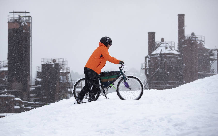 Noah Neighbor pushes his mountain bike up Kite Hill in the snow at Gas Works Park Sunday, Dec. 26, 2021, in Seattle. Snow is blanketing parts of the Pacific Northwest because of unusually cold temperatures.  Seattle got between 3 and 5 inches of snow as of Sunday morning.