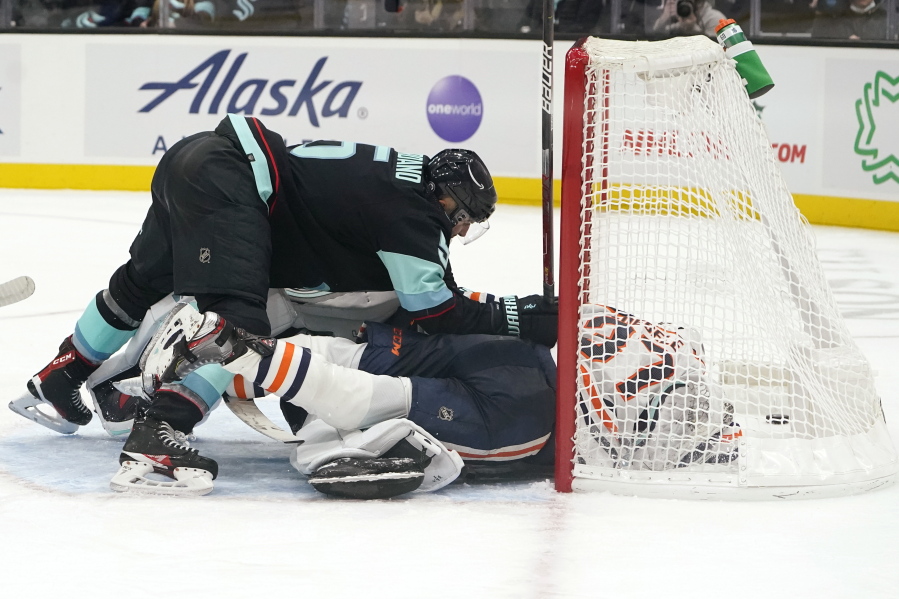 Seattle Kraken's Mark Giordano, left, tumbles atop Edmonton Oilers' Warren Foegele (37) while Kraken goalie Chris Driedger is buried below as the puck sits in the back of the net in the third period of an NHL hockey game Saturday, Dec. 18, 2021, in Seattle. The play was eventually ruled a goal by Foegele.