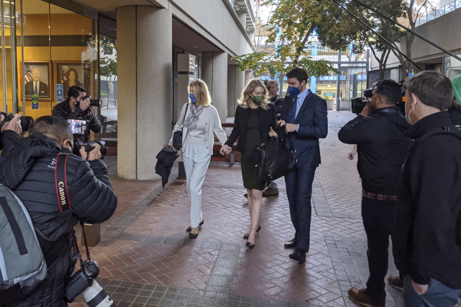 Elizabeth Holmes, center, enters the Robert F. Peckham Federal Building with her partner, Billy Evans, right, and her mother, Noel Holmes, in San Jose, Calif., on Tuesday, Dec. 7, 2021. Looking on at far right is John Carreyrou, the former Wall Street Journal reporter who wrote the October 2015 story that exposed flaws in Theranos' blood-testing technology.
