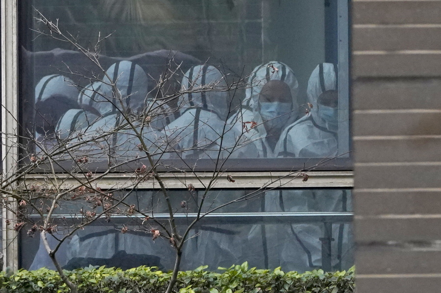 FILE - Members of a World Health Organization team are seen through a window wearing protective gear during a field visit to the Hubei Animal Disease Control and Prevention Center for another day of field visit in Wuhan in central China's Hubei province, on Feb. 2, 2021. Nearly two years into the COVID-19 pandemic, the origin of the virus tormenting the world remains shrouded in mystery.
