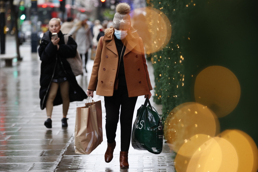 A woman wearing a face mask to guard against COVID-19 carries bags of shopping along Oxford Street in London, Monday, Dec. 27, 2021. In Britain, where the omicron variant has been dominant for days, government requirements have been largely voluntary and milder than those on the continent, but the Conservative government said it could impose new restrictions after Christmas.