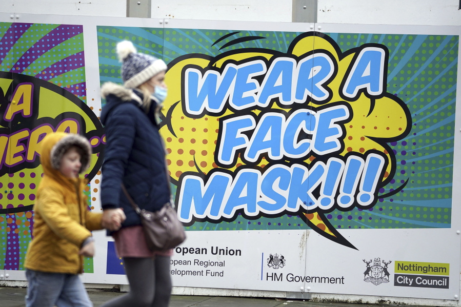 People walk past a billboard inviting citizens to wear face masks to curb the spread of COVID-19, in Nottingham, England, Monday Dec. 20, 2021. Britain's health secretary has refused to rule out imposing tougher COVID-19 restrictions before Christmas amid the rapid rise of infections and continuing uncertainty about the omicron variant.