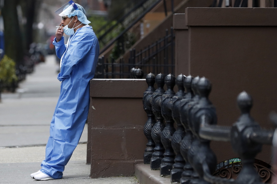 FILE - Emergency room nurse Brian Stephen leans against a stoop as he takes a break from his work at the Brooklyn Hospital Center, Sunday, April 5, 2020, in New York. The worldwide surge in coronavirus cases driven by the new omicron variant is the latest blow to already strained hospitals, nursing homes, police departments and supermarkets struggling to maintain a full contingent of nurses, police officers and other essential workers as the pandemic enters its third year.