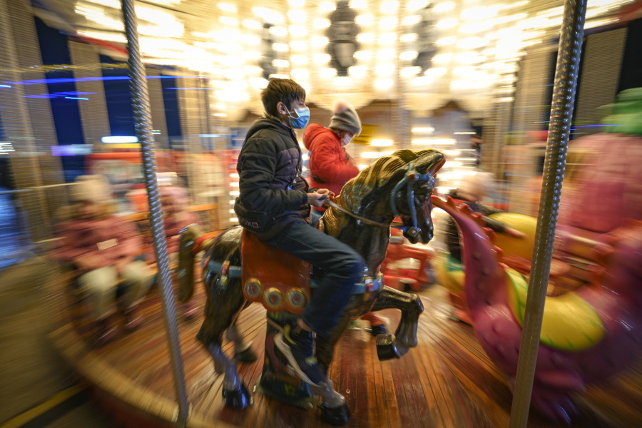 Children, some wearing face masks, enjoy a carousel ride at a Christmas fair in Bucharest, Romania, Saturday, Nov. 27, 2021. The Romanian capital will have three Christmas fairs open for public in the coming weeks and access to the venues will be conditioned by a COVID-19 green pas, proving the holder's vaccination or recovery after the infection.