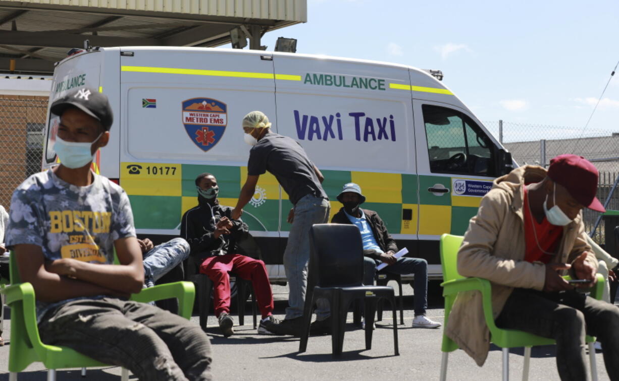 People wait to be vaccinated by a member of the Western Cape Metro EMS (Emergency Medical Services) at a mobile "Vaxi Taxi" which is an ambulance converted into a mobile COVID-19 vaccination site in Blackheath in Cape Town, South Africa, Tuesday, Dec. 14, 2021. The omicron variant appears to cause less severe disease than previous versions of the coronavirus, and the Pfizer vaccine seems to offer less defense against infection from it but still good protection from hospitalization, according to an analysis of data from South Africa, where the new variant is driving a surge in infections.