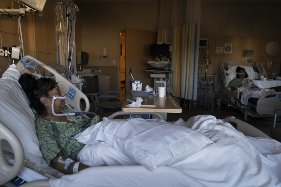 Natalie Balli, 71, and her twin sister, Linda Calderon, background right, watch TV as they rest in their beds in a COVID-19 unit at Providence Holy Cross Medical Center in Los Angeles, Friday, Dec. 17, 2021. The sisters were admitted to the hospital on the same day, a few days after their Thanksgiving gathering. (AP Photo/Jae C.