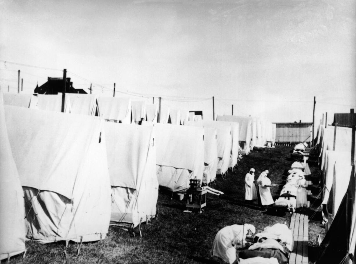 Masked doctors and nurses treat flu patients lying on cots and in outdoor tents at a hospital camp during the influenza epidemic of 1918.