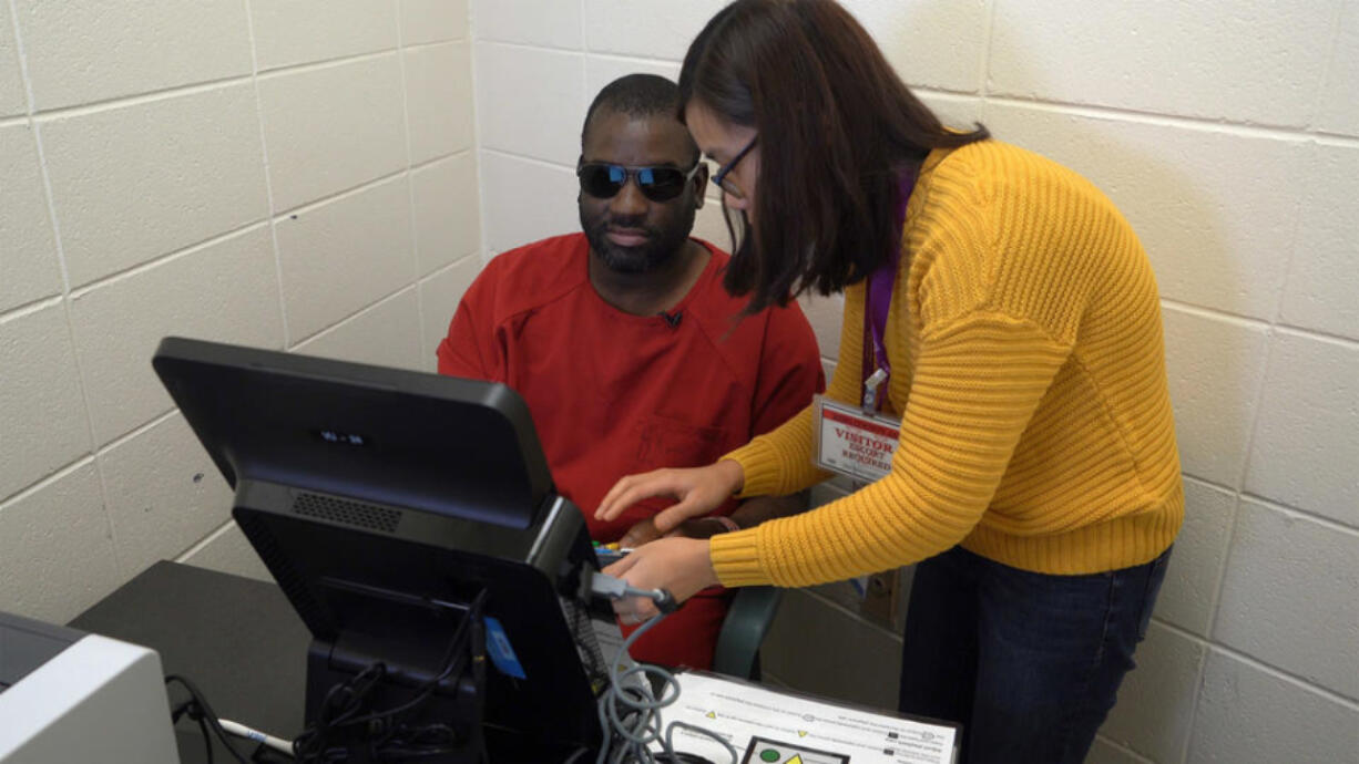Language Services and Community Engagement Specialist at King County Elections Nhien Huynh assists Jordan Landry, who is visually impaired, as he uses an Accessible Voting Unit to cast a vote in the November 2019 election while incarcerated at King County Correctional Facility.