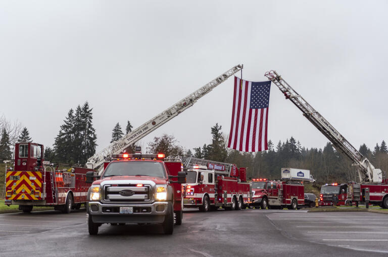 Fire trucks and other emergency response vehicles pass under an American flag on Tuesday, Jan. 18, 2022, at Liberty Bible Church of the Nazarene. The trucks were part of a funeral processional for retired Clark County Fire District 6 firefighter and paramedic Joe Killian, who died from cancer on Jan. 8.
