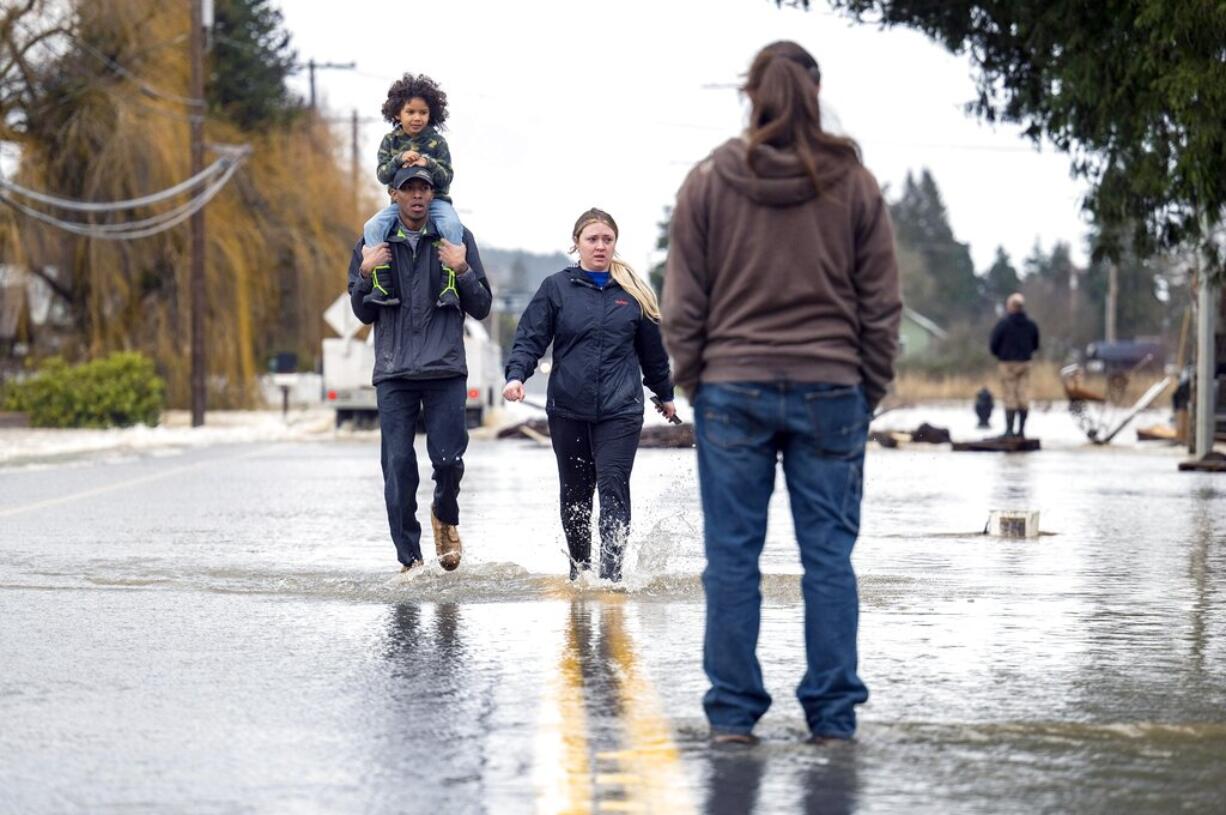 Reggie Brown, of Centralia, carries his daughter, Ocean, 4, on his shoulders as he walks through the floodwaters on Highway 507 with his wife, Jonell Brown, on Friday, Jan. 7, 2022, in Centralia, Wash.