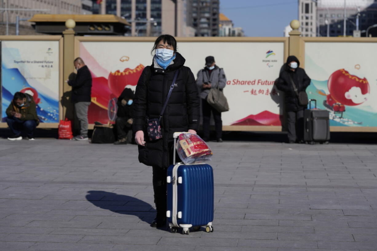 A traveler waits outside the Beijing railway station with her suitcase in Beijing, China, Friday, Jan. 28, 2022. The Beijing Winter Olympics is coinciding with the Chinese Lunar New Year and renewed Covid outbreaks prompting the Chinese authorities to call on the public to stay where they are instead of traveling to their hometowns for the year's most important family holiday.