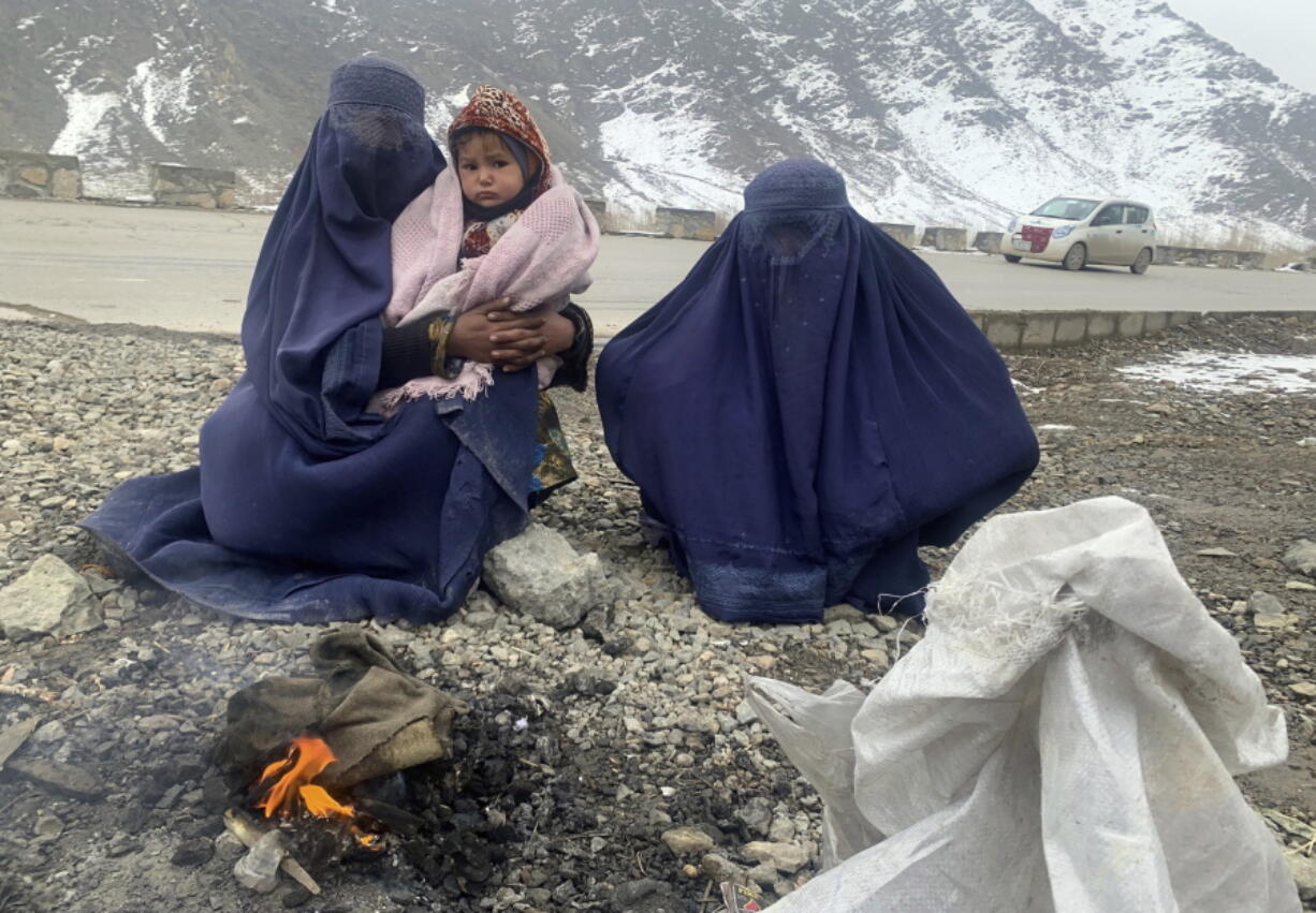 Gulnaz, left, keep her 18-month-old son warm themselves as they wait for alms in the Kabul - Pul-e-Alam highway eastern Afghanistan, Tuesday, Jan. 18, 2022. The Taliban's sweep to power in Afghanistan in August drove billions of dollars in international assistance out of the country and sent an already dirt-poor poor nation, ravaged by war, drought and floods, spiralling toward a humanitarian catastrophe.