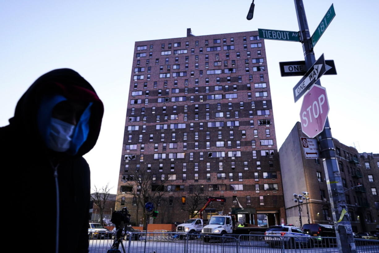 A person walks past an apartment building which suffered the city's deadliest fire in three decades, in the Bronx borough of New York, Tuesday, Jan. 11, 2022.  A malfunctioning electric space heater apparently started the fire Sunday in the 19-story building in the Bronx, fire officials said.