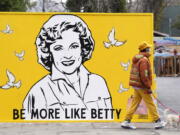 A man walks a dog past a new mural of the late actress Betty White by artist Corie Mattie in Los Angeles.