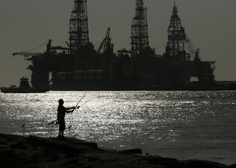 FILE - A man wears a face mark as he fishes near docked oil drilling platforms, on May 8, 2020, in Port Aransas, Texas. A federal court has rejected a proposed lease auction for offshore oil drilling in the Gulf of Mexico, saying the Biden administration failed to conduct a proper environmental review. The decision on Jan. 27, 2022, by U.S. District Judge Rudolph Contreras sends the proposed lease sale back to the Interior Department to decide next steps.
