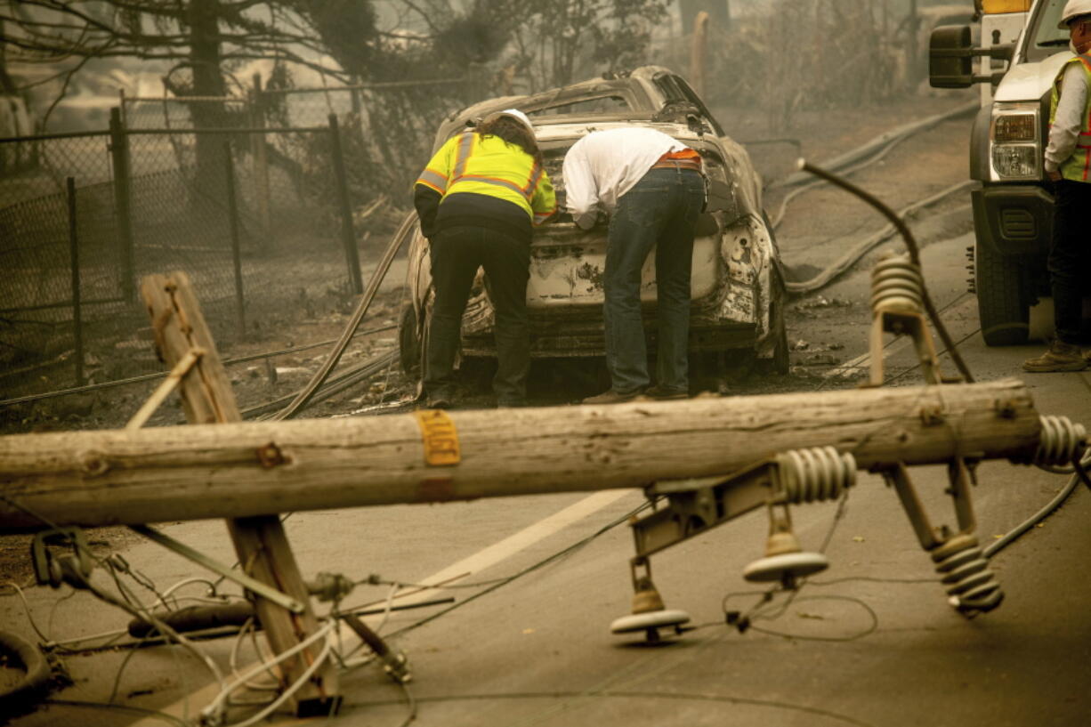 FILE - In this Nov. 10, 2018 file photo, with a downed power utility pole in the foreground, Eric England, right, searches through a friend's vehicle after the wildfire burned through Paradise, Calif. The nation's largest utility, Pacific Gas & Electric is poised to emerge from five years of criminal probation amid worries that it remains too dangerous to be trusted. Over the five years, the utility became an even more destructive force. More than 100 people have died and thousands of homes and businesses have been incinerated in wildfires sparked by its equipment in that time.