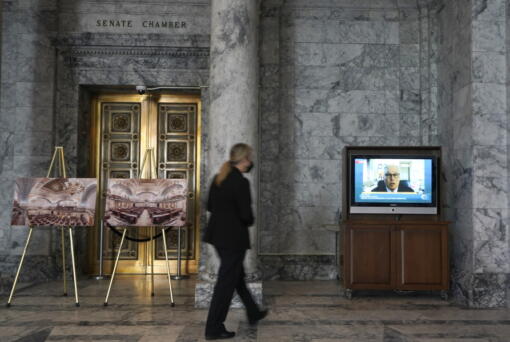A Senate security worker walks near a video display outside the Senate chamber showing Washington Gov. Jay Inslee testifying remotely at a committee hearing on a bill that would make it a gross misdemeanor for elected officials or candidates to knowingly lie about election outcomes if those claims result in violence, Friday, Jan. 28, 2022, at the Capitol in Olympia, Wash. (AP Photo/Ted S.