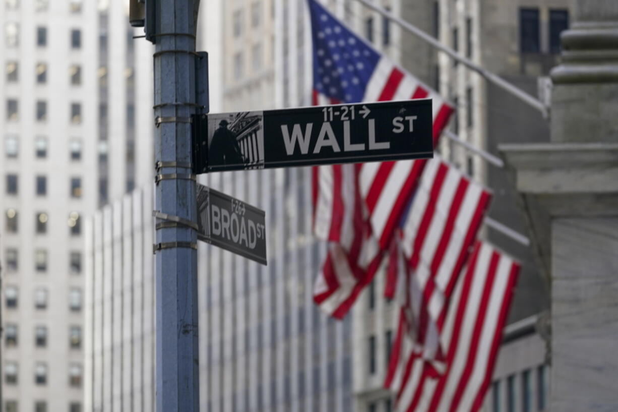 The Wall St. street sign is framed by the American flags flying outside the New York Stock exchange, Friday, Jan. 14, 2022, in the Financial District.  Stocks are opening with solid gains on Wall Street Wednesday, Jan. 26, led by technology stocks after Microsoft reported standout results for its latest quarter.