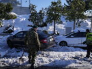 Greek soldiers try to free a vehicle stuck in snow on the Attiki Odos motorway, following Tuesday's heavy snowfall, in Athens, on Wednesday, Jan. 26, 2022.