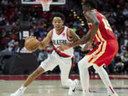 Portland Trail Blazers guard Anfernee Simons, left, dribbles around Atlanta Hawks center Clint Capela during the second half of an NBA basketball game in Portland, Ore., Monday, Jan. 3, 2022.