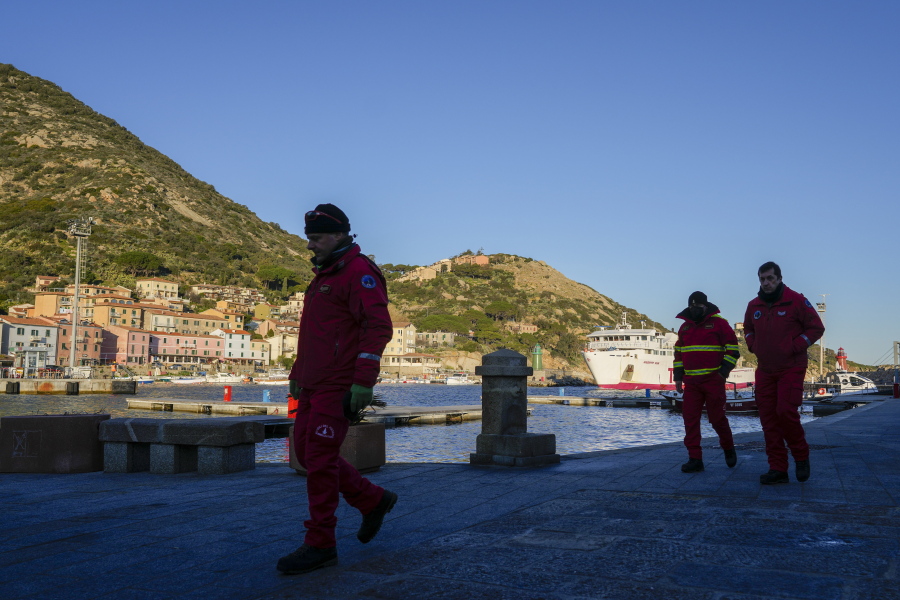 Firefighters walk on a pier of the port of the tiny Tuscan island of Isola del Giglio, Italy, as a ferry boat enters it, Thursday, Jan. 13, 2022. Italy on Thursday is marking the 10th anniversary of the Costa Concordia cruise ship disaster with a daylong commemoration, honoring the 32 people who died but also the extraordinary response by the residents of Giglio who took in the 4,200 passengers and crew from the ship on that rainy Friday night and then lived with the Concordia carcass for another two years before it was hauled away for scrap.